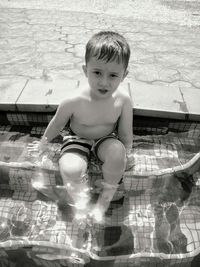 Portrait of shirtless boy sitting in swimming pool