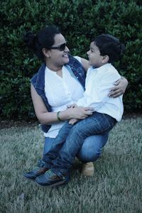 Happy mother with son crouching on grassy field against plant