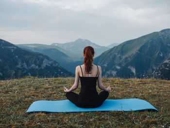 Full length of woman sitting on mountain against sky