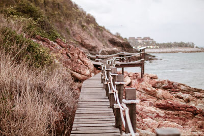 Wooden footbridge over sea against sky