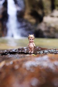 Close-up of figurine on rock against waterfall