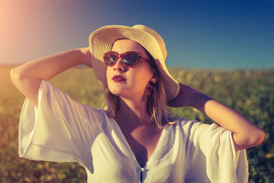 Beautiful young woman wearing sunglasses standing on land against sky