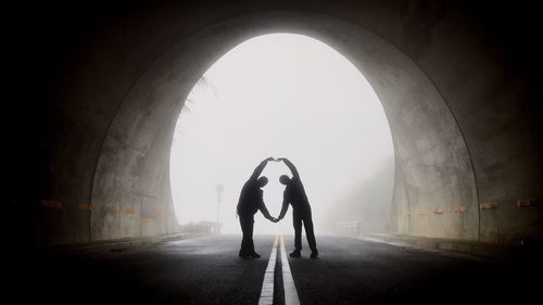 Silhouette friends gesturing while standing in tunnel during foggy weather