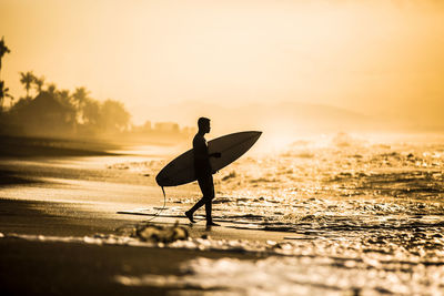 Silhouette man with surfboard on beach during sunset