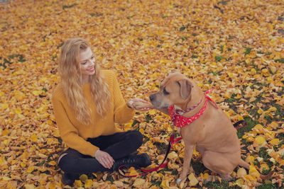 Woman with dog sitting on autumn leaves