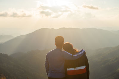 Rear view of couple looking at mountains against cloudy sky