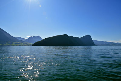 Scenic view of sea and mountains against clear blue sky