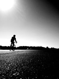 Silhouette man riding bicycle on street against sky