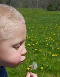 Close-up of boy with yellow dandelion flower on field