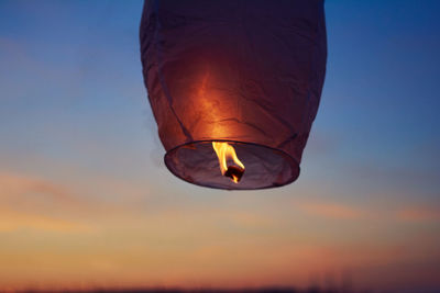 Low angle view of illuminated fire lantern against sky at sunset