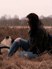 Woman sitting with pug on grassy field