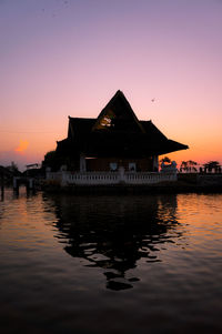 Silhouette buildings by lake against sky during sunset