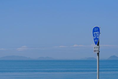 Information sign by sea against blue sky