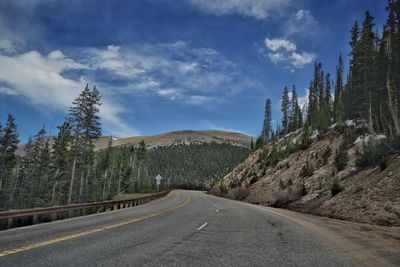 Diminishing perspective of empty road amidst trees against blue sky