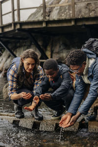 Parents and son collecting water in hands while crouching near stream