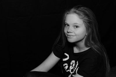 Close-up portrait of smiling young woman against black background