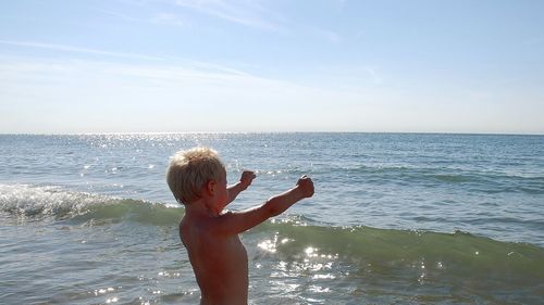 Shirtless boy standing at sea against sky