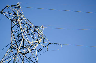 Low angle view of electricity pylon against blue sky