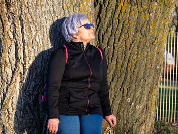 Senior woman standing against tree trunk