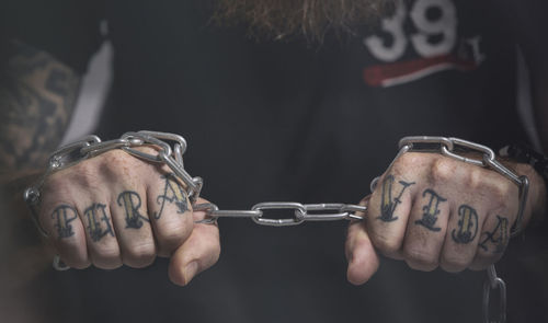 Closer up man in black clothes stands upright and holds a rusty metal chain, a concept of strength