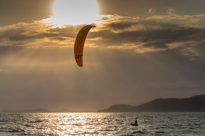 Man kiteboarding in sea against sky during sunset