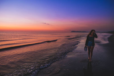 Woman standing on beach against sky during sunset