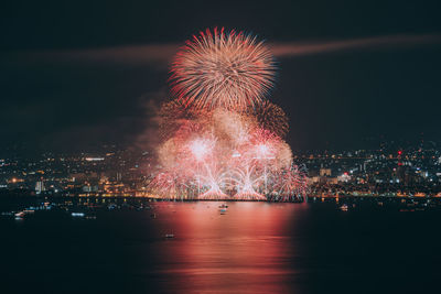 Firework display over illuminated city against sky at night