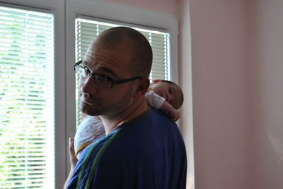 Portrait of father carrying toddler son against window at home