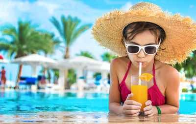 Girl wearing straw hat drinking orange juice at poolside