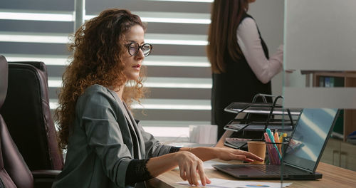 Two coworkers silently working in office one on laptop the other with folders. 