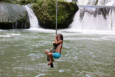 Portrait of boy hanging from rope against waterfall