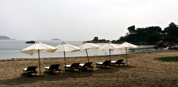 Lounge chairs and parasols on beach against clear sky