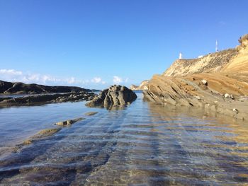 Rock formations on shore against clear blue sky