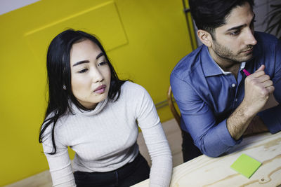 Tilt image of woman and man looking away while sitting at desk in creative office