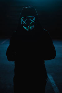 Close-up of man wearing mask standing in darkness