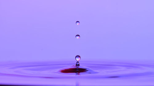 Close-up of drop falling on water against blue background