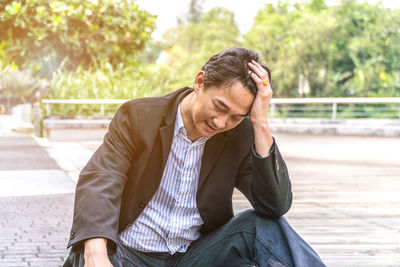 Stressed man with head in hand sitting at public park