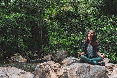 Young woman sitting on rock against trees in forest