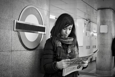 Young woman reading newspaper while standing by text on metal