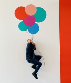 Side view of man holding colorful balloons against white background