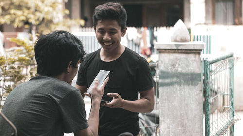 Young man holding smart phone while standing outdoors