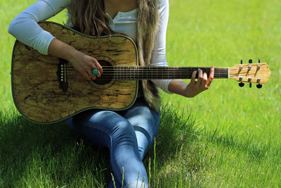 Midsection of woman playing guitar while sitting in park