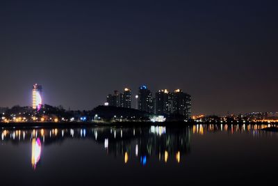 Illuminated buildings by lake against sky at night