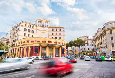 Cars on city street by buildings against sky