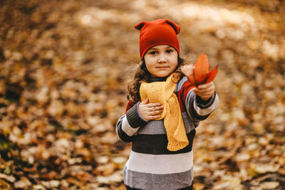 Portrait of a little girl a child in a warm hat walking holding an autumn leaf in forest outdoors