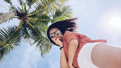 Low angle view of young woman on palm tree against sky