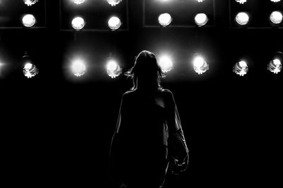 Rear view of woman standing against illuminated lights at night