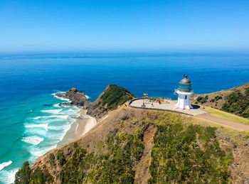 Lighthouse by sea against clear blue sky