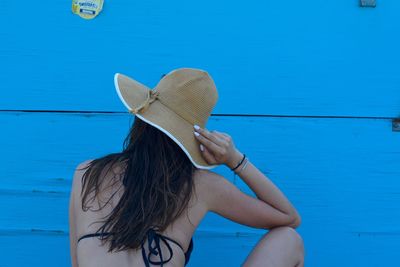 Rear view of woman wearing hat standing against blue wall
