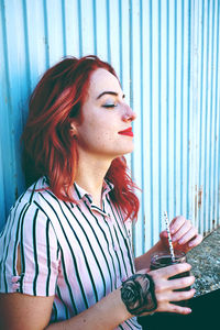 Woman having drink while sitting by wall